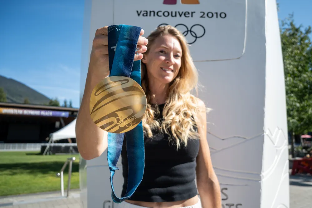 McIvor holds her gold medal to the camera in front of a monument for the 2010 Olympics in Whistler.