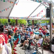 A crowd of people seated under a white tent with various countries' flags draped across the ceiling.