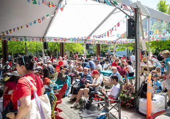 A crowd of people seated under a white tent with various countries' flags draped across the ceiling.