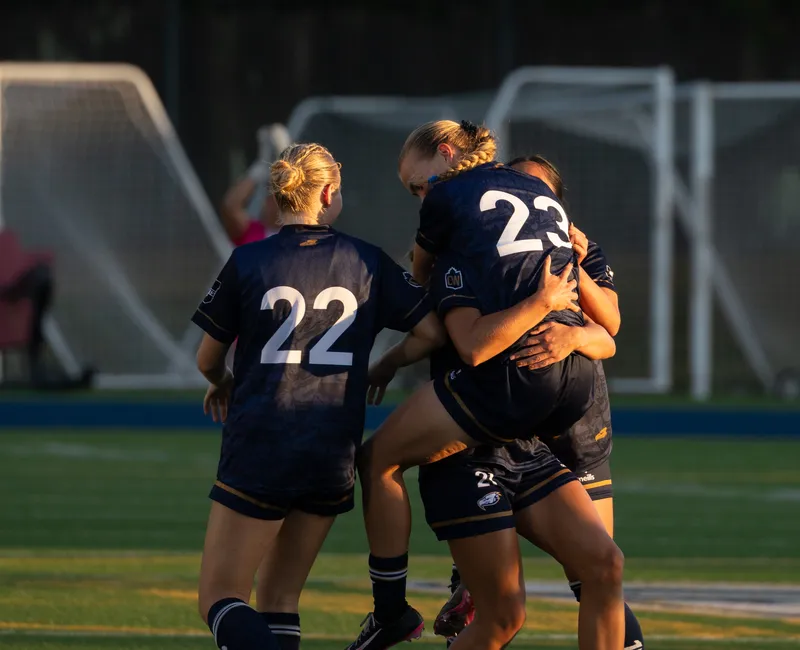Norman jumps into the arms of her teammates, celebrating together.