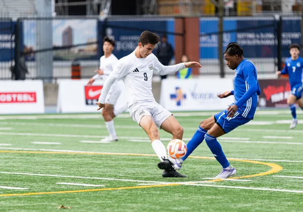A T-Bird in white and a Carabin in blue kick the ball at the same time from opposite sides.