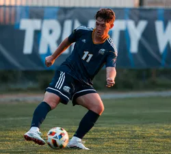 Brennen Fuerst dribbles the ball as the sun sets, wearing a blue Thunderbirds jersey