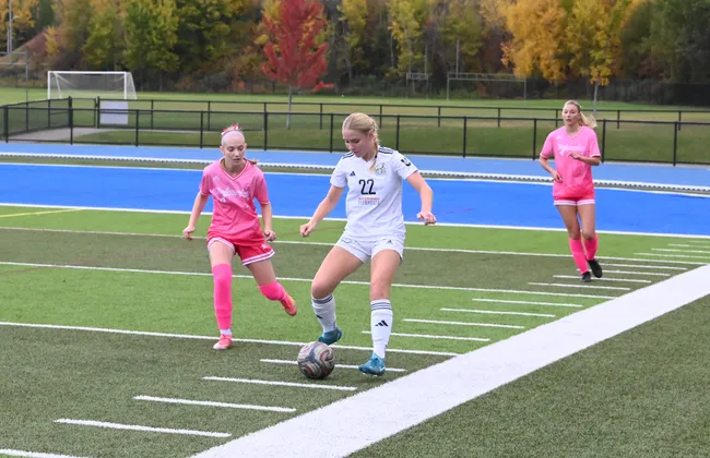 A UBC player controls the ball with two defenders in pink jerseys nearby.