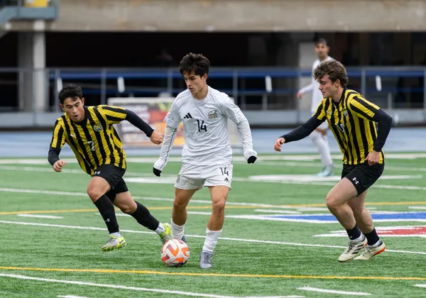 A T-Bird in a white jersey runs with the ball, with Dalhousie players in black and yellow vertical striped jerseys on both sides of him.