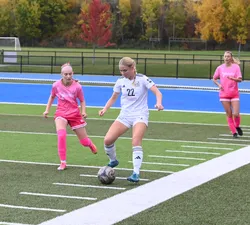 A UBC player controls the ball with two defenders in pink jerseys nearby.