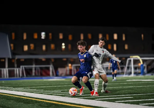 At night, a UBC player in blue turns his back to a Toronto player in white to keep him from stealing the ball.