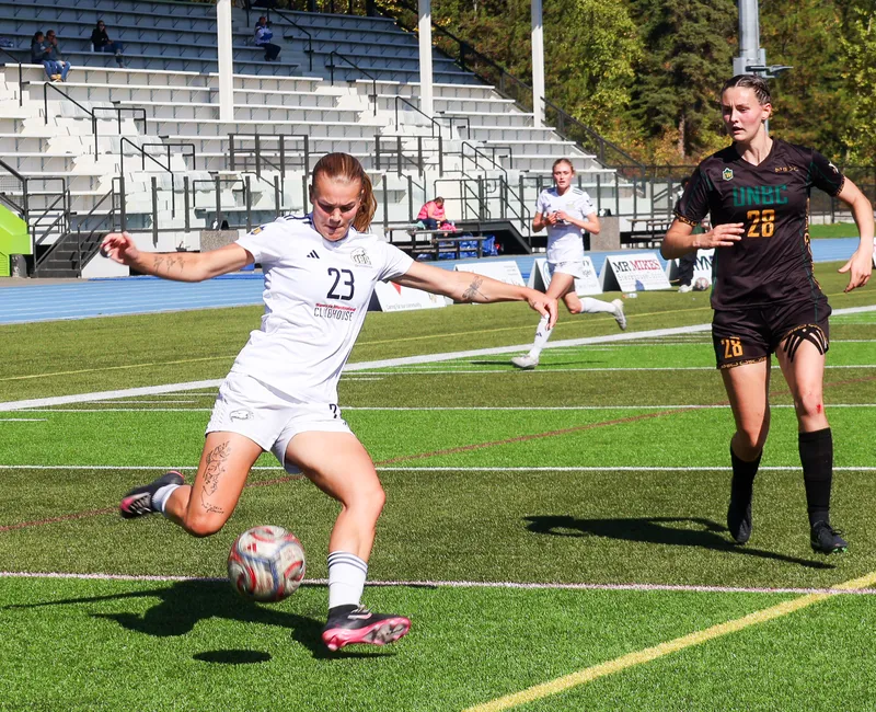 Norman, in a white T-Birds jersey, takes a shot with a defender in a brown jersey behind her.