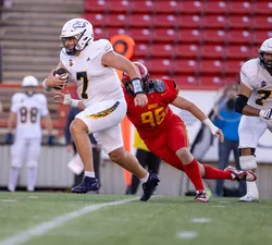 Viotto tucks the ball and runs, wearing a white jersey, running past a diving Dino in a red jersey.