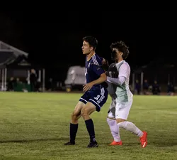 Comsia, in blue, receives a pass with a UFV defender in white pressed against his back.