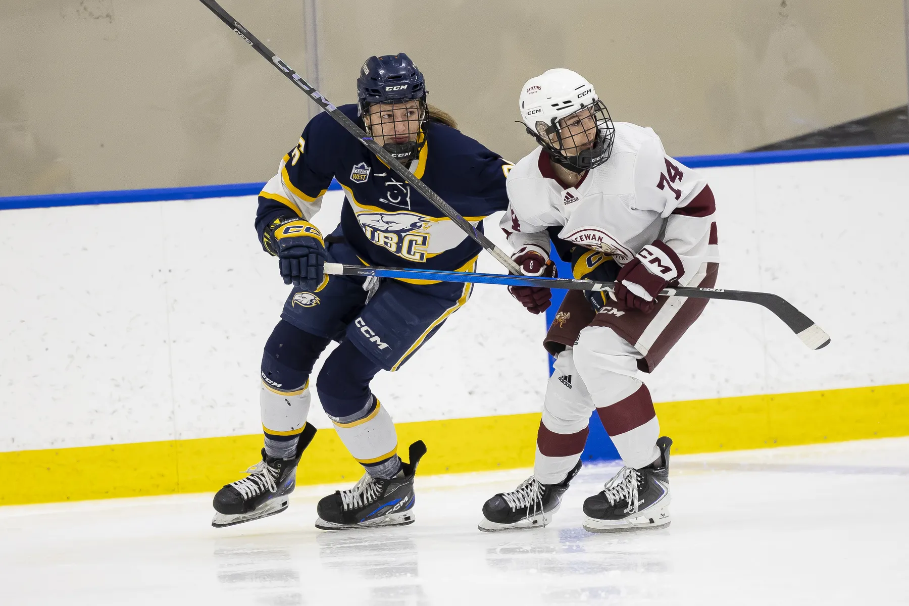A Thunderbird in a blue and white jersey tries to skate past a MacEwan player in white and red.
