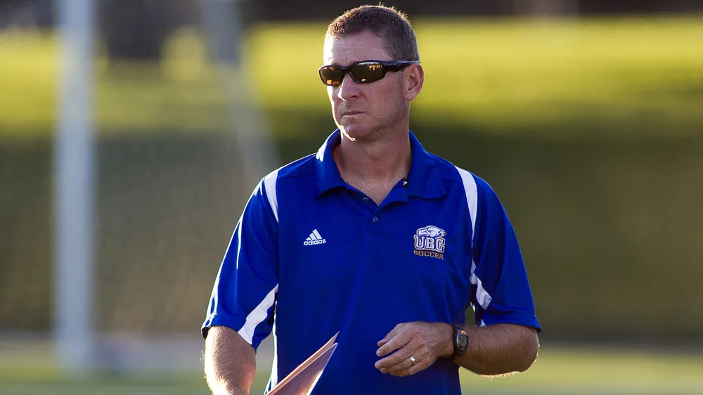 A younger Mike Mosher stands on the field in a blue Thunderbirds shirt.
