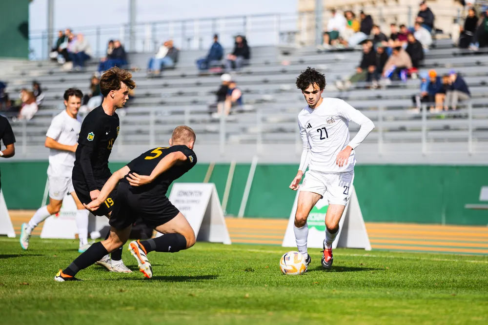 UBC player dribbles UAlberta players on the field
