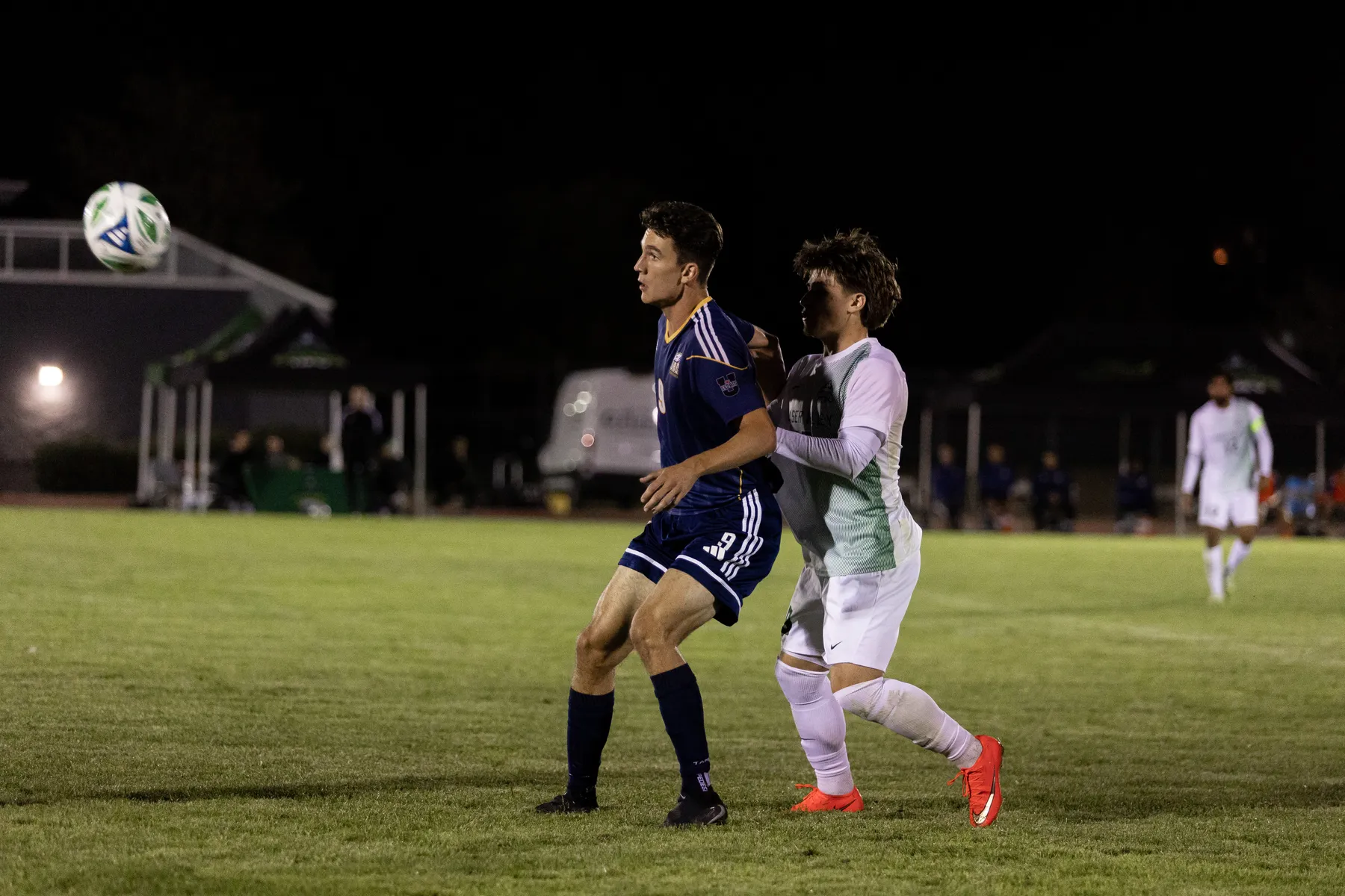 Comsia, in blue, receives a pass with a UFV defender in white pressed against his back.