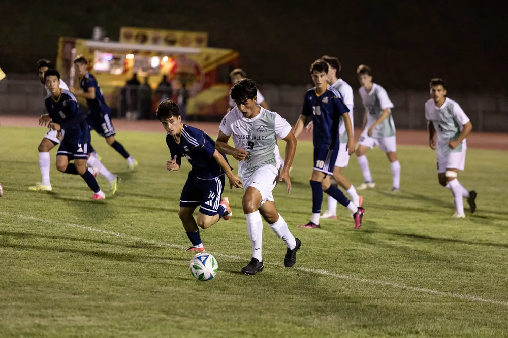 A UFV player runs up field with the ball, being pursued by multiple UBC defenders.