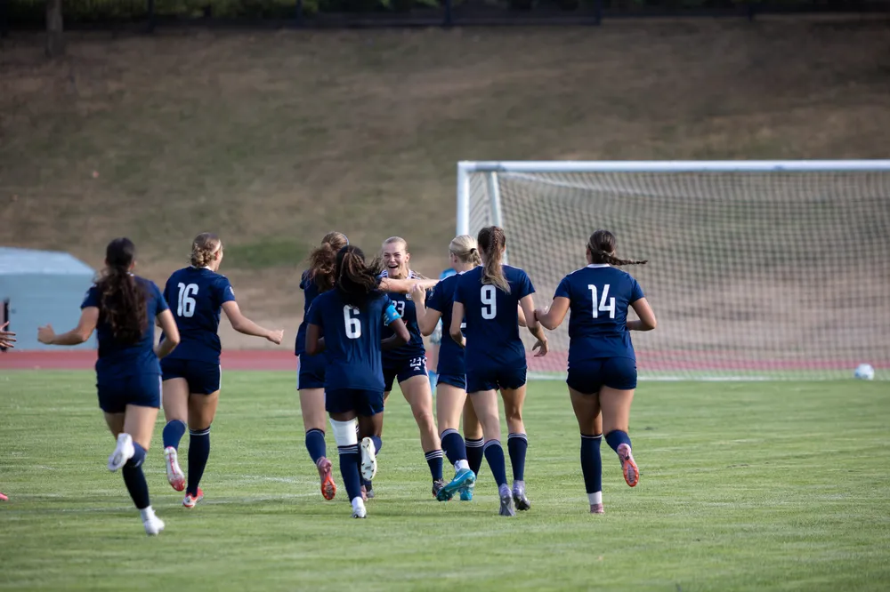 A UBC player celebrates scoring a goal with her teammates.