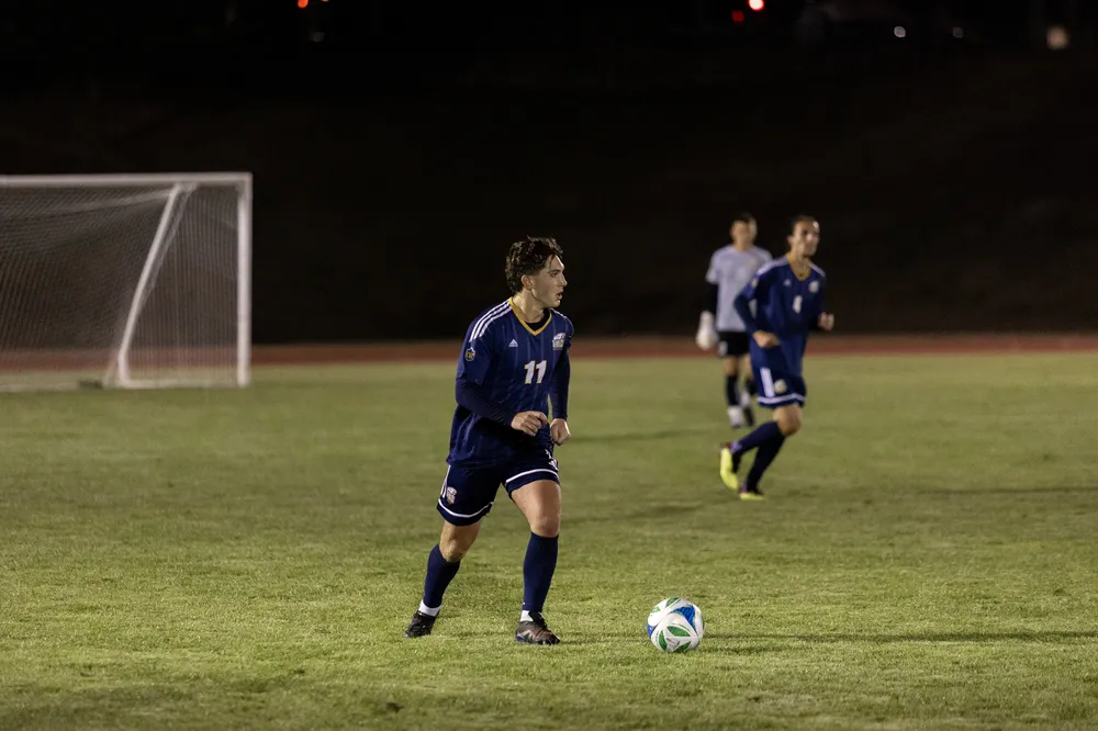 A UBC player stands in the backfield with the ball at his feet.