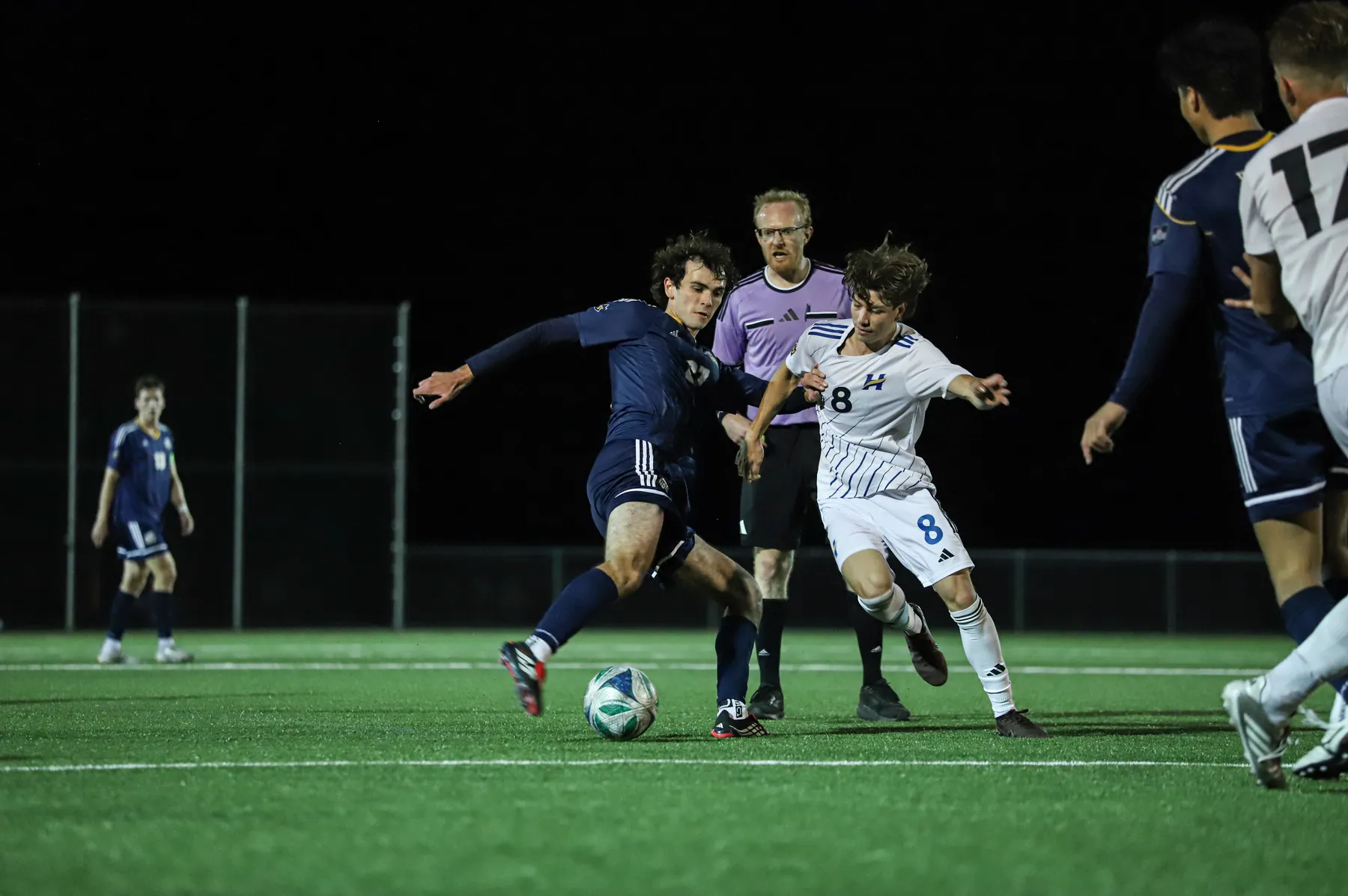 A UBC and UBCO player grapple for possession of the ball as the referee looks over.