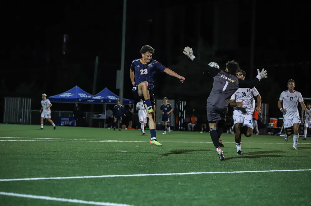 A UBC player takes a shot on goal, while the UBCO goalie jumps out to contest.