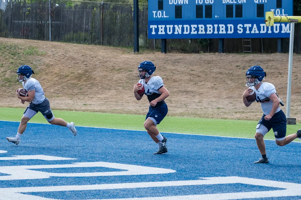 Three UBC players in practice gear run out of the end zone.