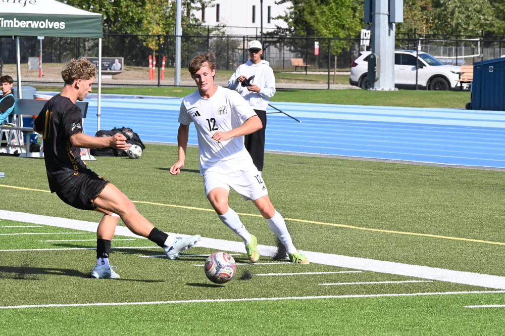 A UBC player tries to dribble around a UNBC defender.