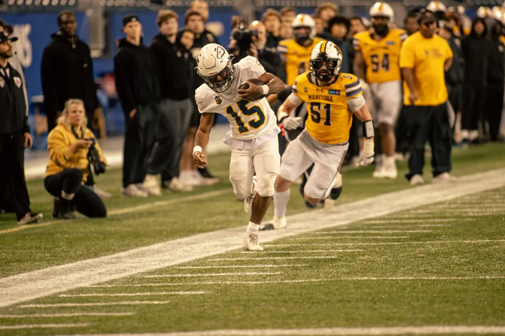 A UBC player tows the sideline with the football, while being chased by a Mantioba defender