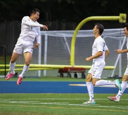 Yuan jumps up in the air and celebrates as his teammates chase him, all wearing white jerseys.