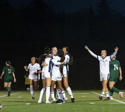 UBC, in white jerseys, celebrates together after scoring a goal.