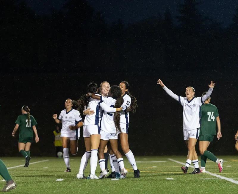UBC, in white jerseys, celebrates together after scoring a goal.