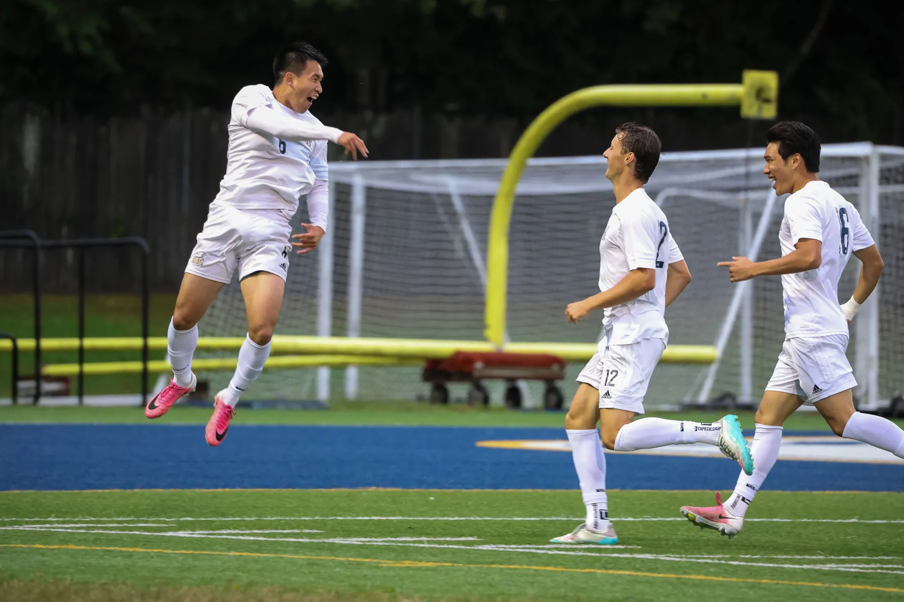 Yuan jumps up in the air and celebrates as his teammates chase him, all wearing white jerseys.