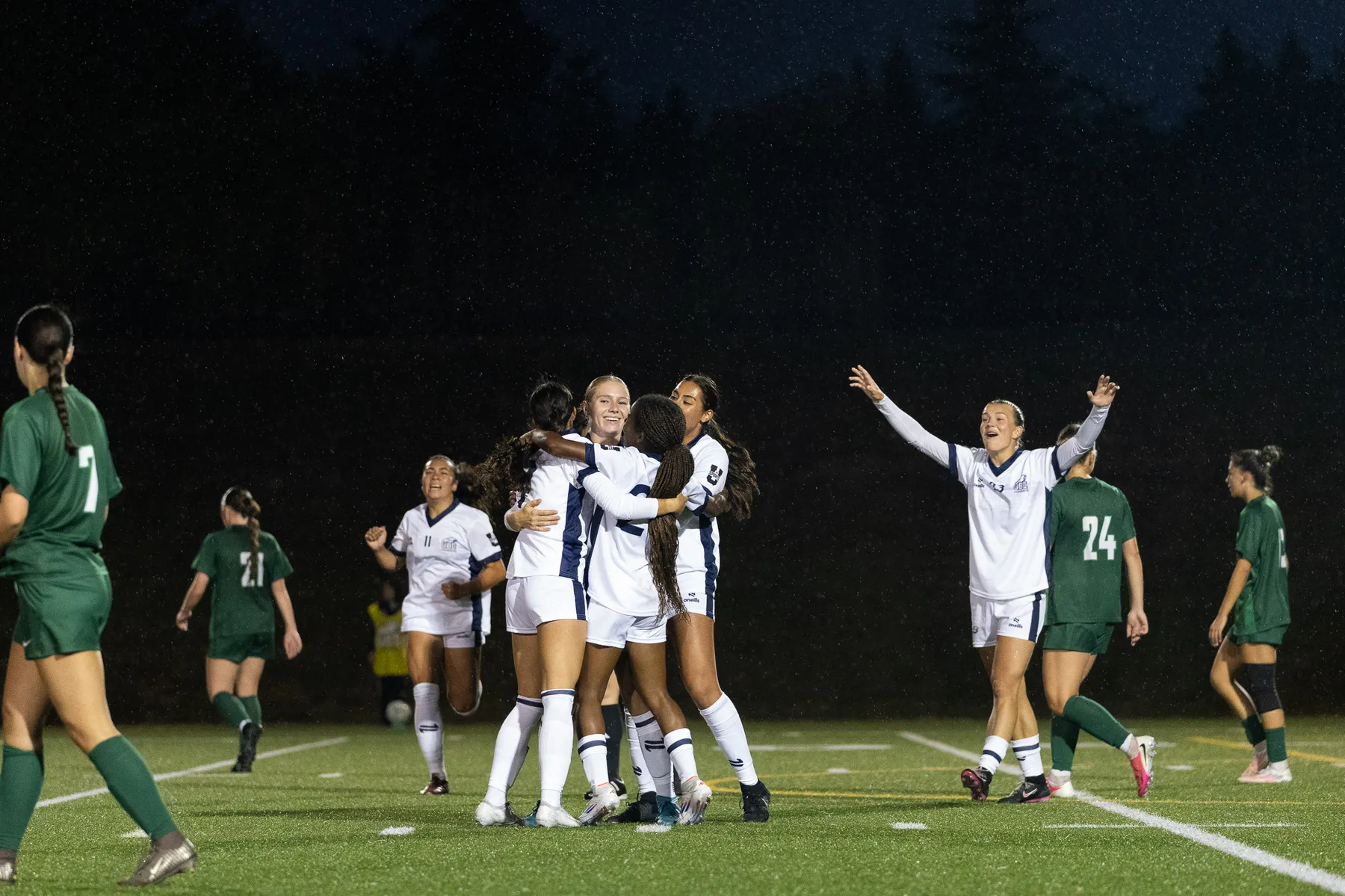 UBC, in white jerseys, celebrates together after scoring a goal.
