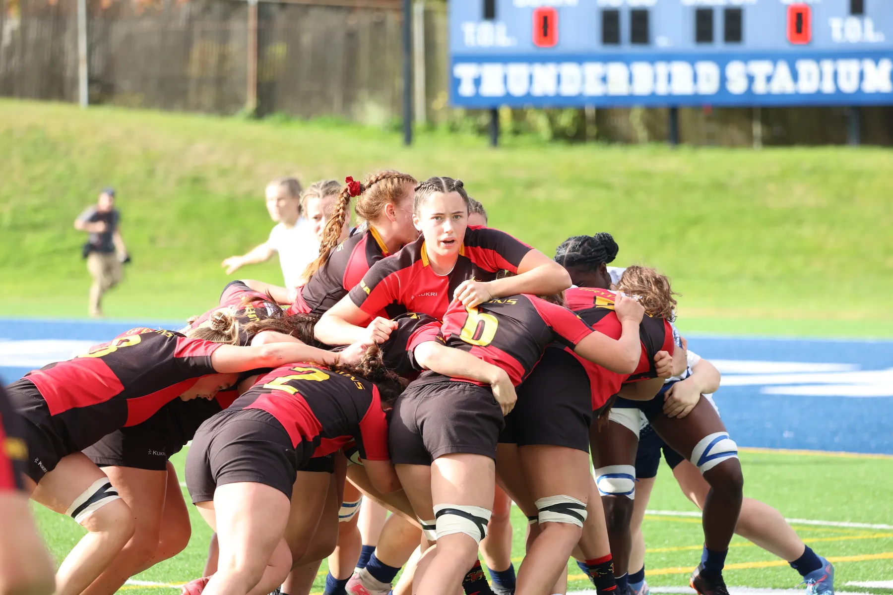 A group of Gryphons in red and black push a pile of bodies towards the end zone, which is visible behind them.