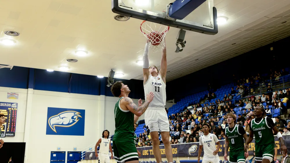Gauthier hangs off the rim after a dunk against UFV, with the War Memorial crowd in the background.