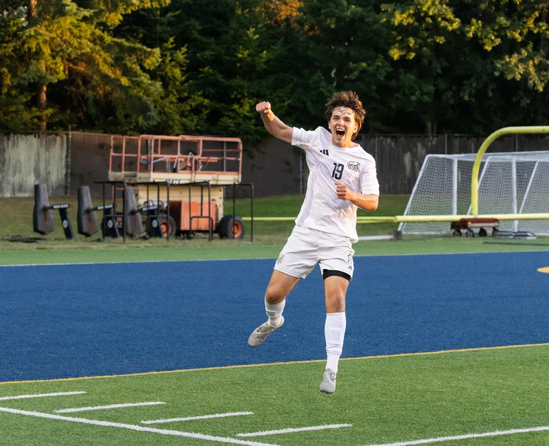 A UBC player in a white jersey jumps up in the air, pumping his fist in celebration.