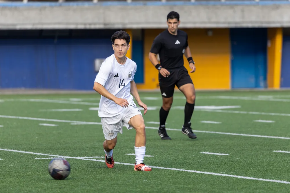 Herbert dribbles the ball up the field, with a referee behind him.