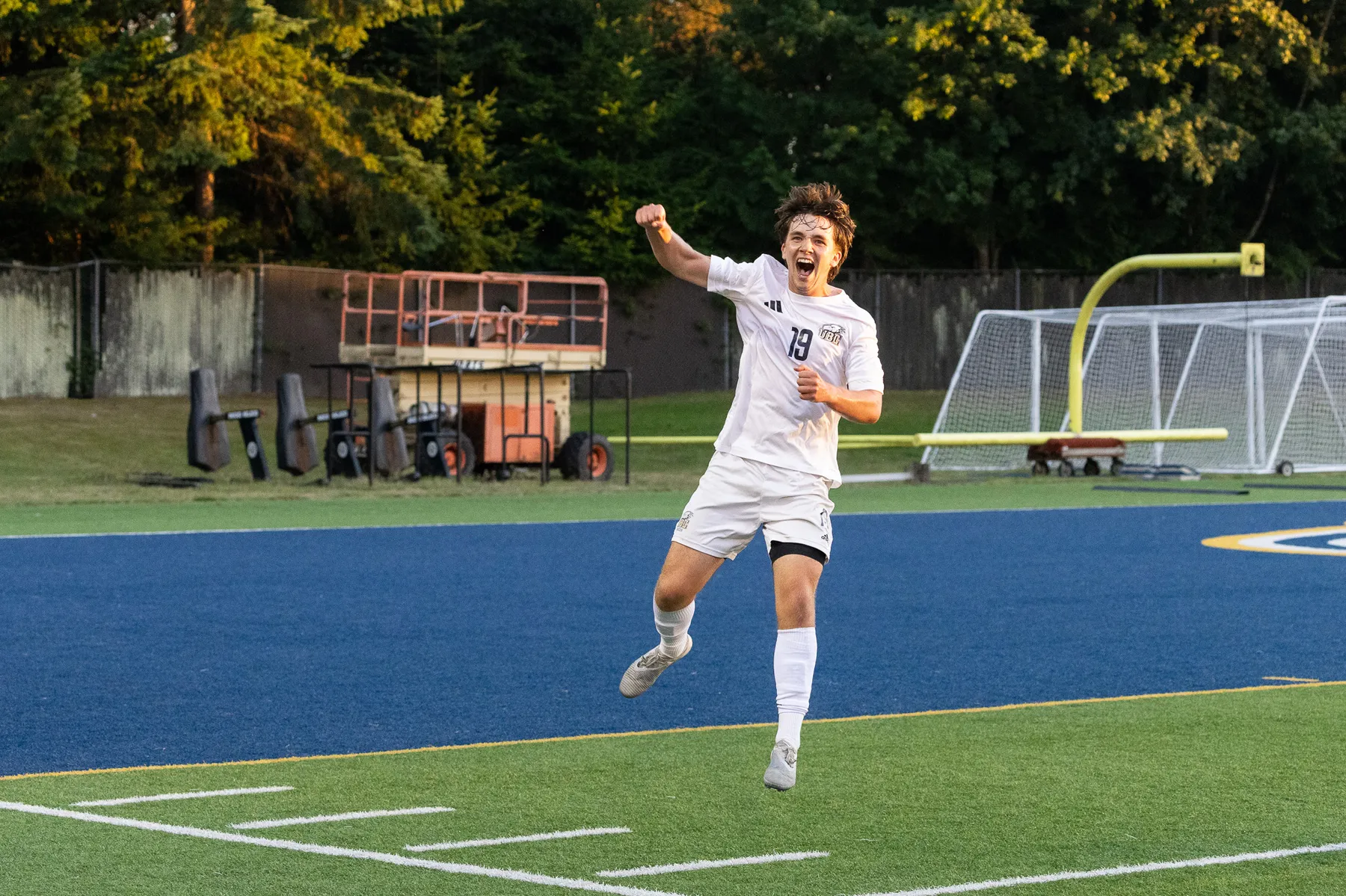 A UBC player in a white jersey jumps up in the air, pumping his fist in celebration.