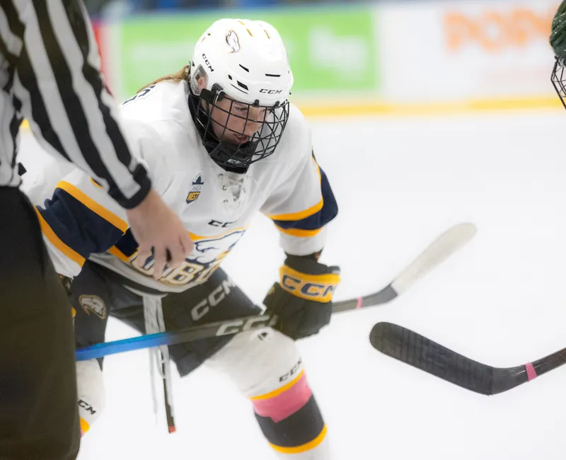 With a referee on the left side of the photo holding on to the puck, a T-Bird in white lines up against a Panda in black, ready to start play.