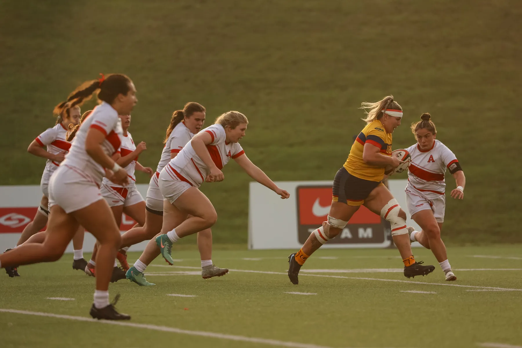 Surrounded by Acadia players in white and red, a Gael in yellow runs upfield.