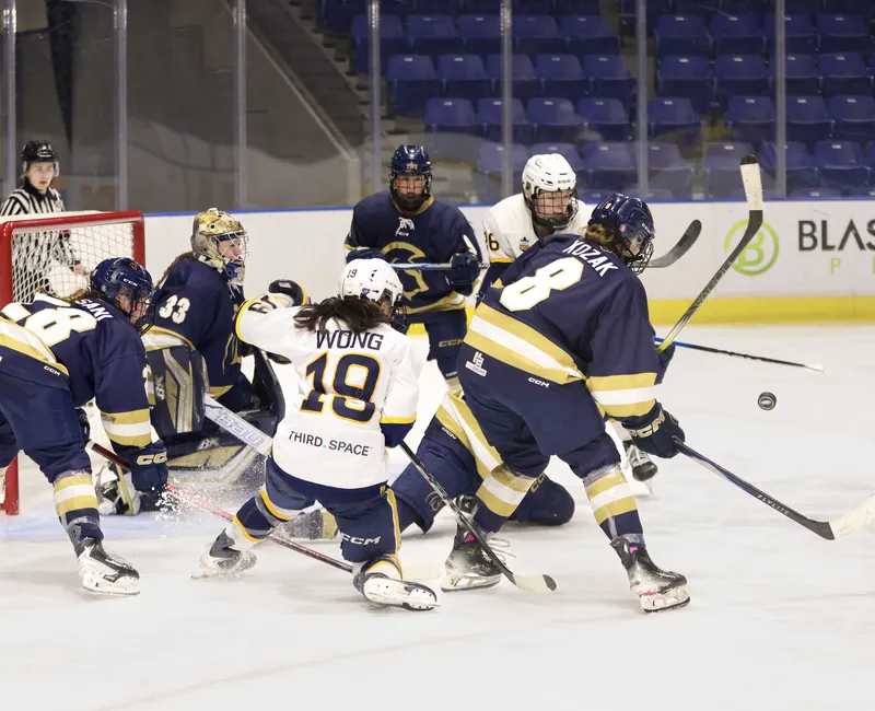 A goalmouth scramble forms in front of the TWU net, with the Spartans in dark blue and the T-Birds in white.