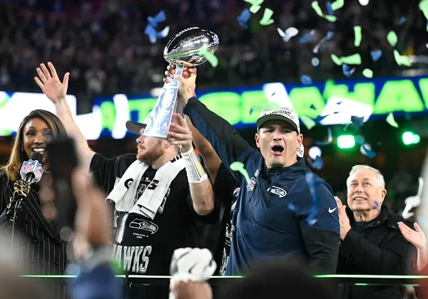 As confetti falls, a man holds a trophy above his head.
