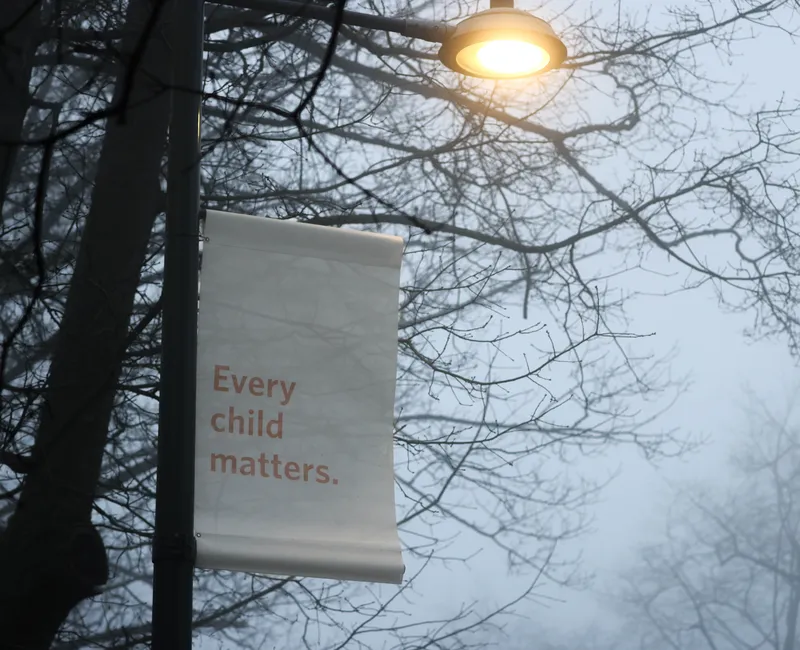 Attached to a street light, a banner stating "every child matters" hangs in the fog.