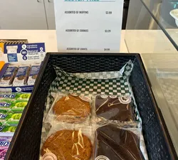 A basket of cookies individually wrapped in plastic with a sign reading "gluten-free" and a list of baked goods and their prices.