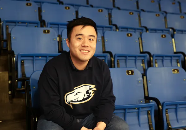 A headshot of Oskar Ho wearing a navy Thunderbird sweatshirt in a seat in gym bleachers.