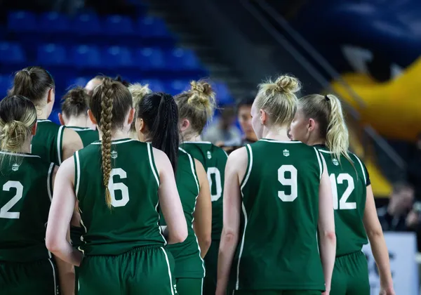 A group of woman basketball players in green jerseys with their backs turned.