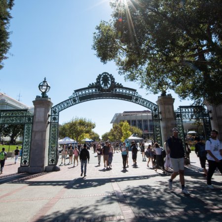 Color photo of about five people walking through Sather Gate on a sunny day, viewed from the middle distance