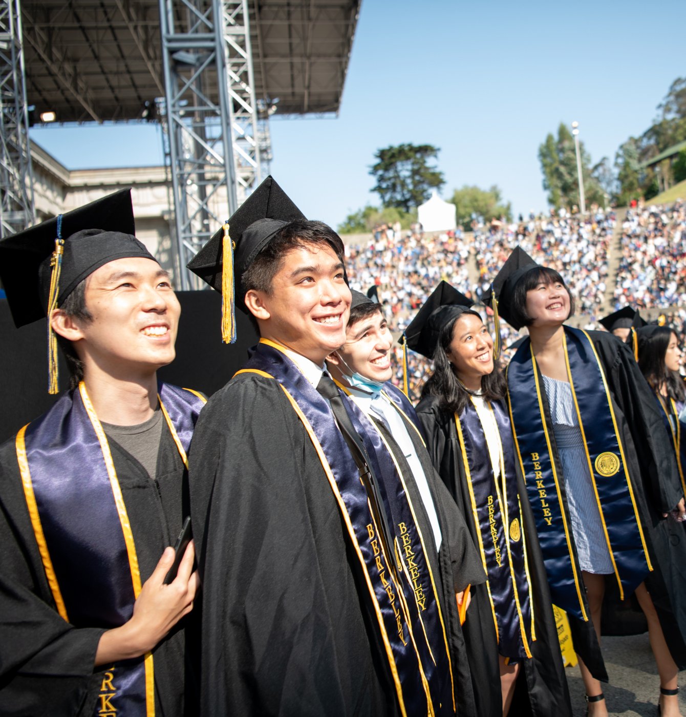 A group of graduates in regalia is smiling and looking upward toward the sky.