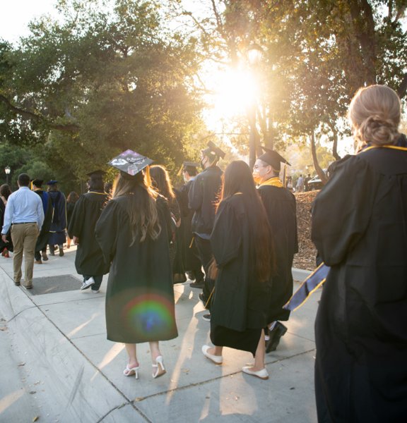 Graduates walking into the Greek Theatre with the sun peering through the trees.