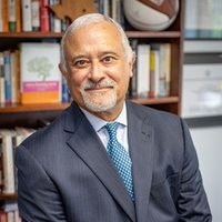 Photo of Luis H. Zayas in front of bookshelves wearing a suit and tie