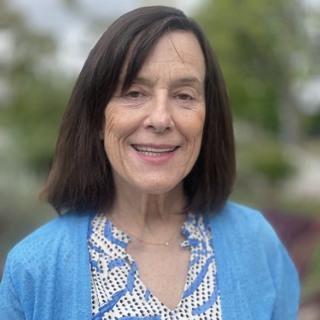 Color photo of Janis smiling at the camera in a blue and white blouse under a light blue cardigan