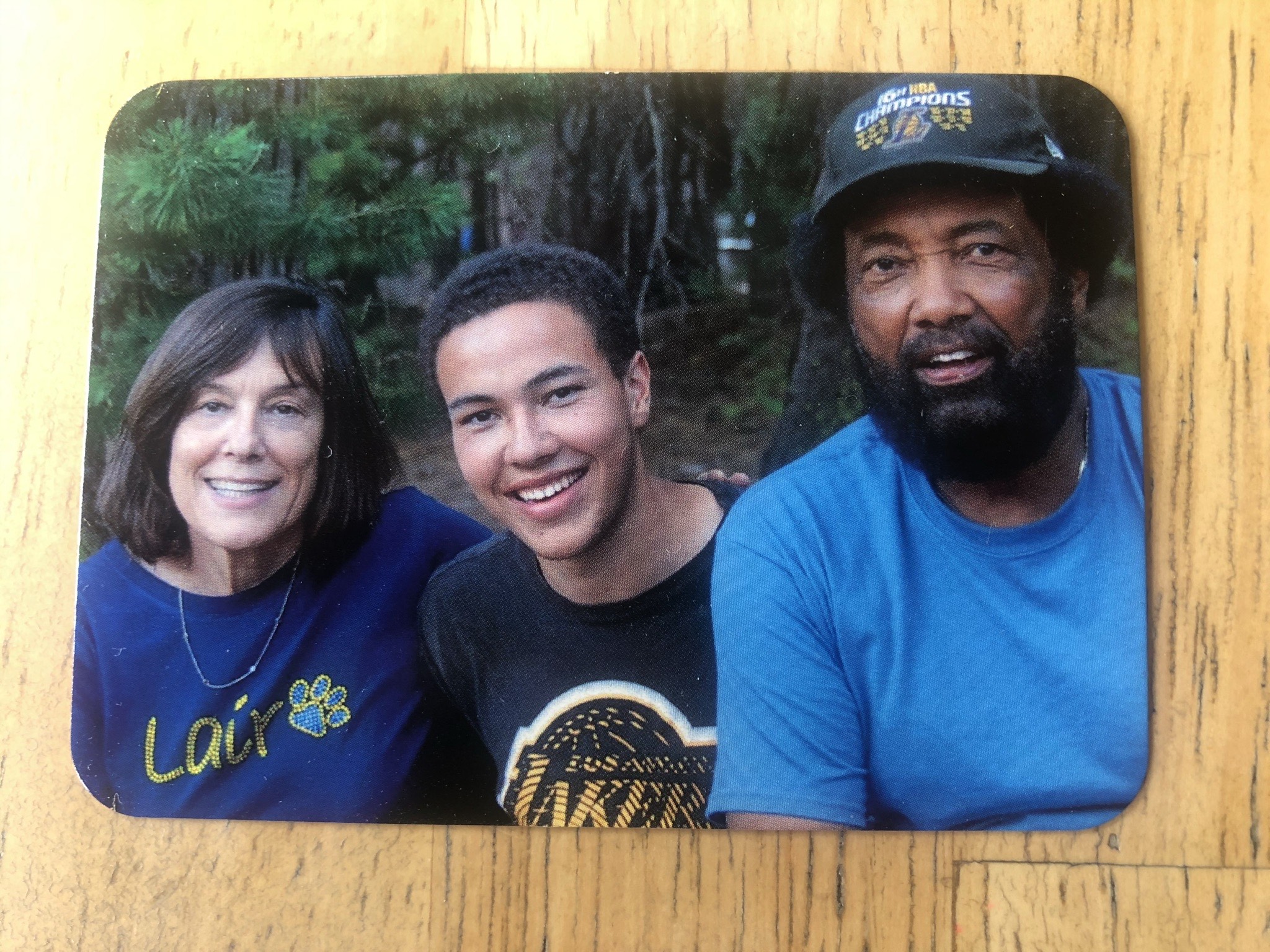 Color photo of a family of three wearing blue and gold t-shirts, trees behind them