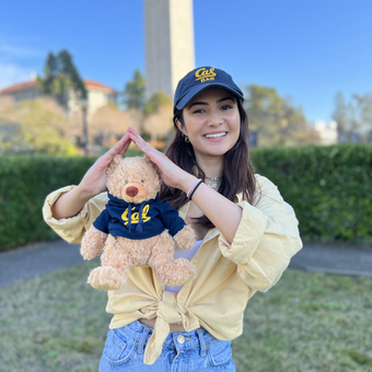 Color photo of Cal Student Philanthropy Club Member and Housing the Bears Ambassador Danees Chaudhry holding a stuffed bear on front of the Campanile!